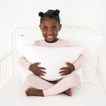 Young girl holding a soft white pillow in a white toddler bed