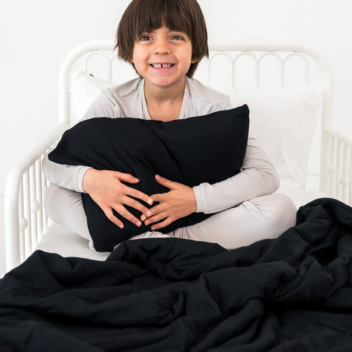 Child holding a black pillow on a bed with a black blanket