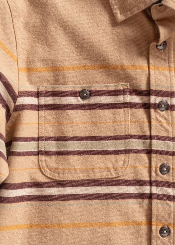 Close-up of a beige flannel shirt with brown and yellow stripes, featuring a buttoned chest pocket and collar detail.
