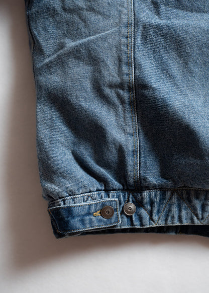 Close-up of a blue denim jacket's hem with two metal buttons on a white background, highlighting texture and stitching details.