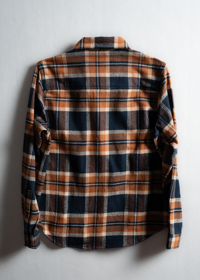 A plaid flannel shirt in orange and navy is laid flat on a white background, showcasing its back and checkered pattern.