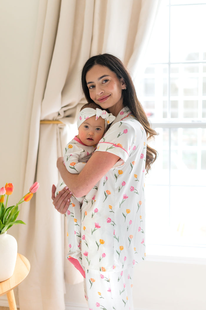 Female model wearing the Women's Short Sleeve Cropped Pajama Set in Tulip holding toddler matching in a footie