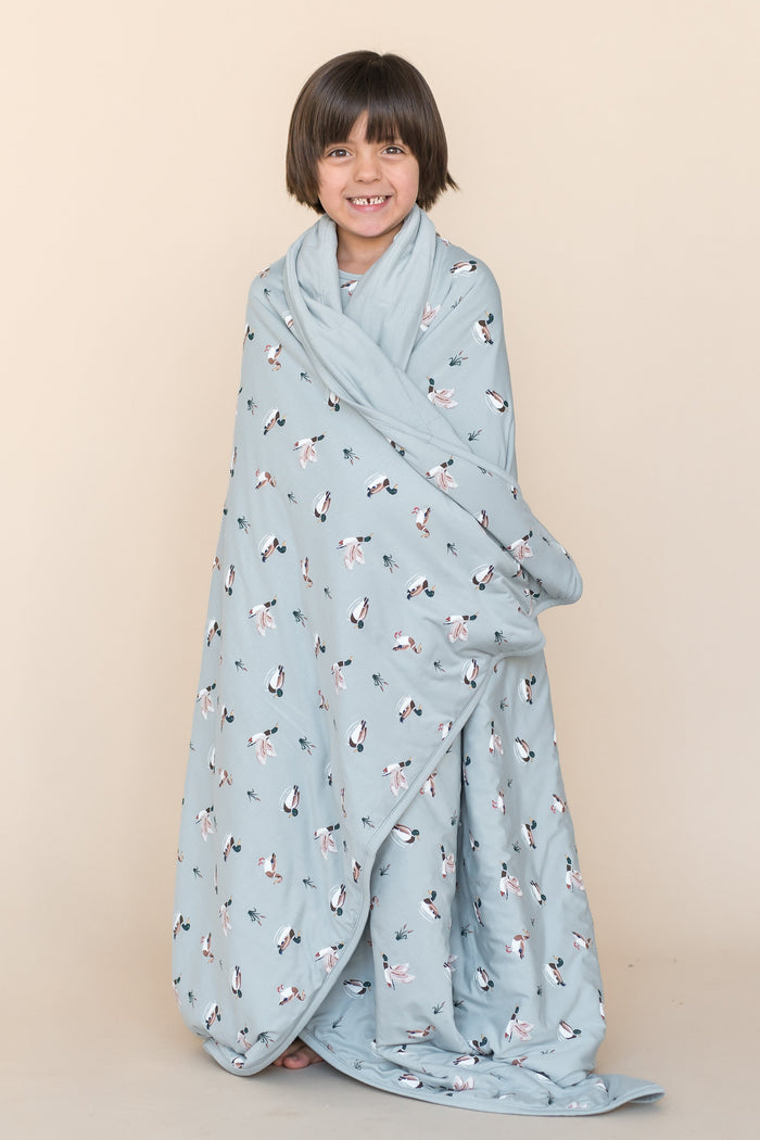 Young smiling boy standing wearing the Youth Blanket in Mallard Duck 1.0 around his shoulders