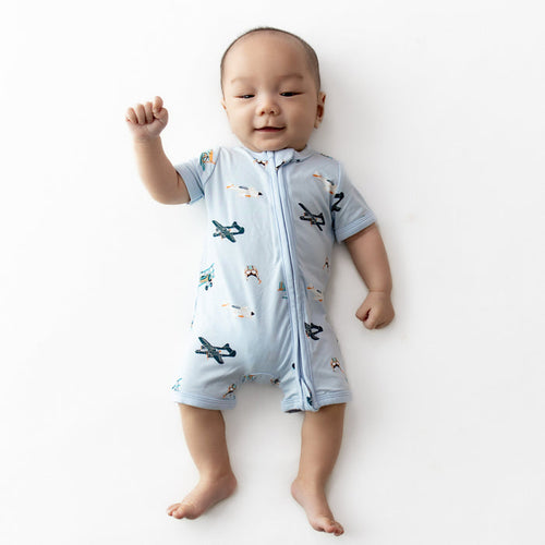 Young infant laying down wearing the Zipper Shortall Romper in Take Off