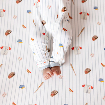 The zipper closure on the leg of the Zippered Romper in Home Run shown on an infant model laying on a Crib Sheet in Home Run