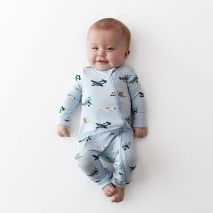 Smiling infant laying on a white surface wearing the Zippered Romper in Take Off